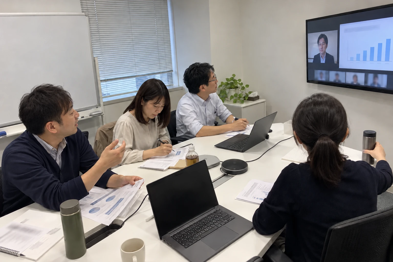 会議室でオンライン勉強会に参加し、資料を見ながら意見を交わす会員
